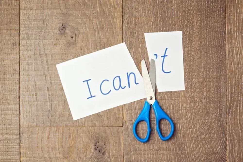 A pair of scissors is cutting a piece of paper that says `` i can 't ''.