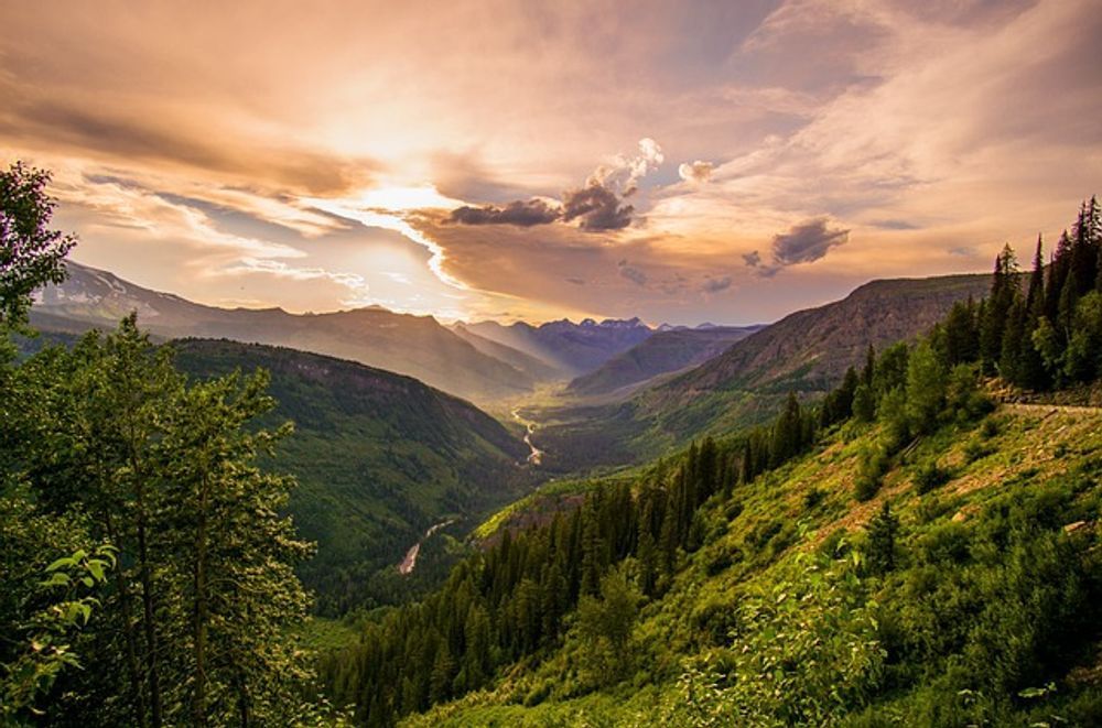 A view of a valley surrounded by mountains and trees at sunset.