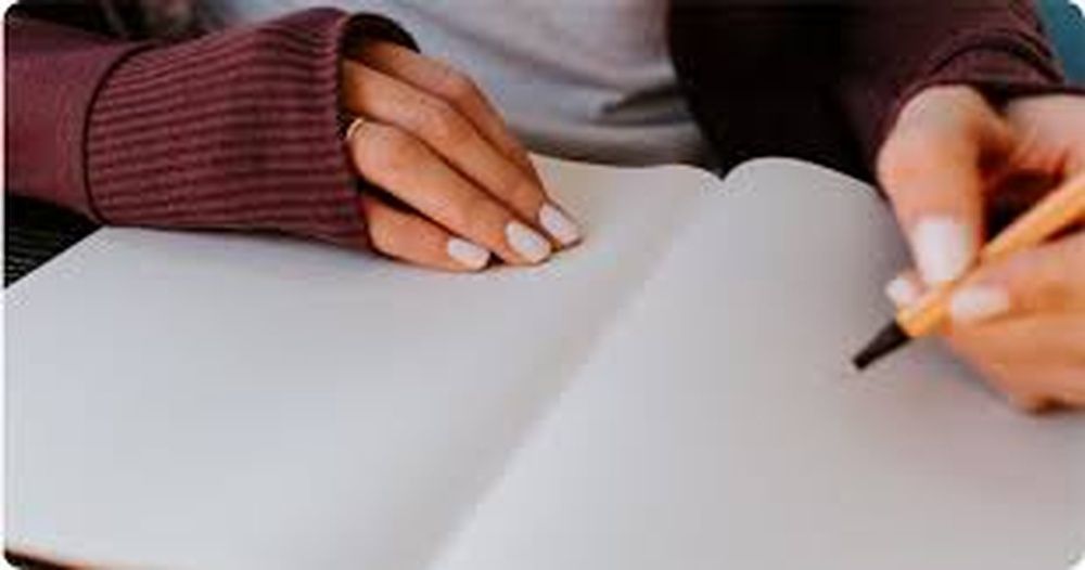 A woman is writing in a notebook with a pencil.