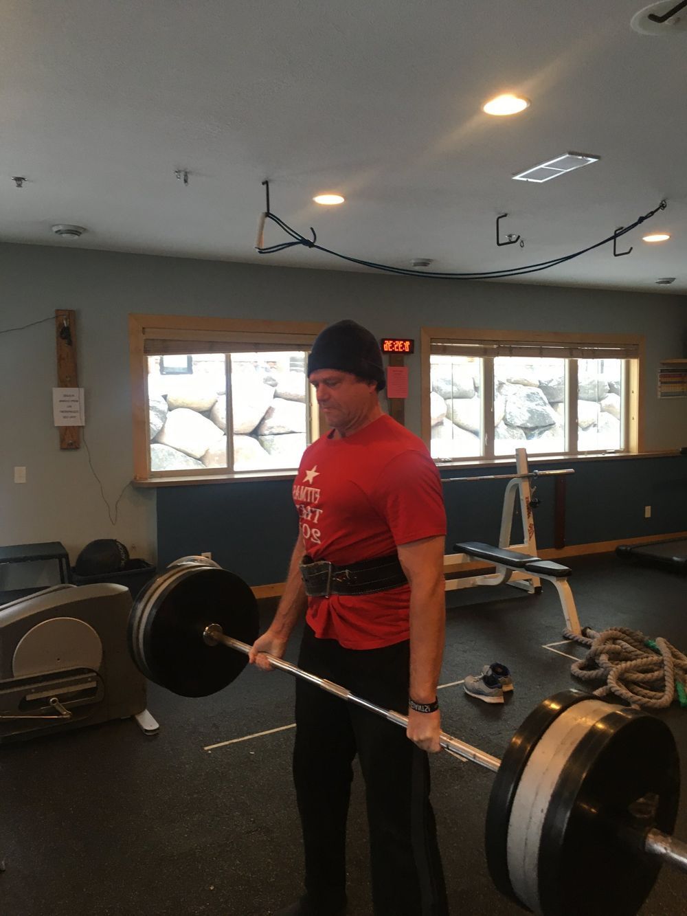 A man in a red shirt is lifting a barbell in a gym