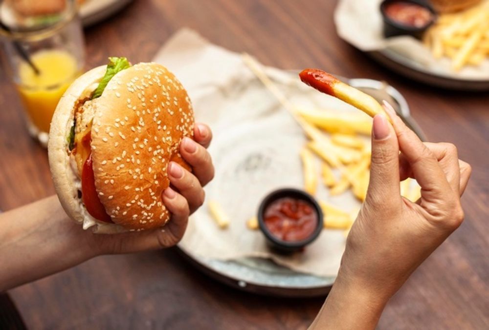 A person is holding a hamburger and french fries in their hands.