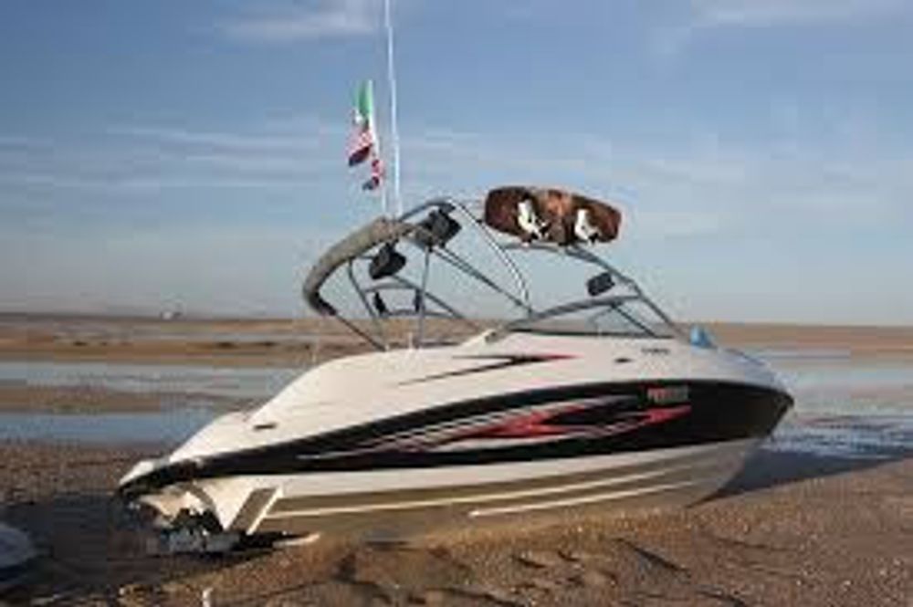 A boat with a wakeboard on top of it is sitting on the beach.