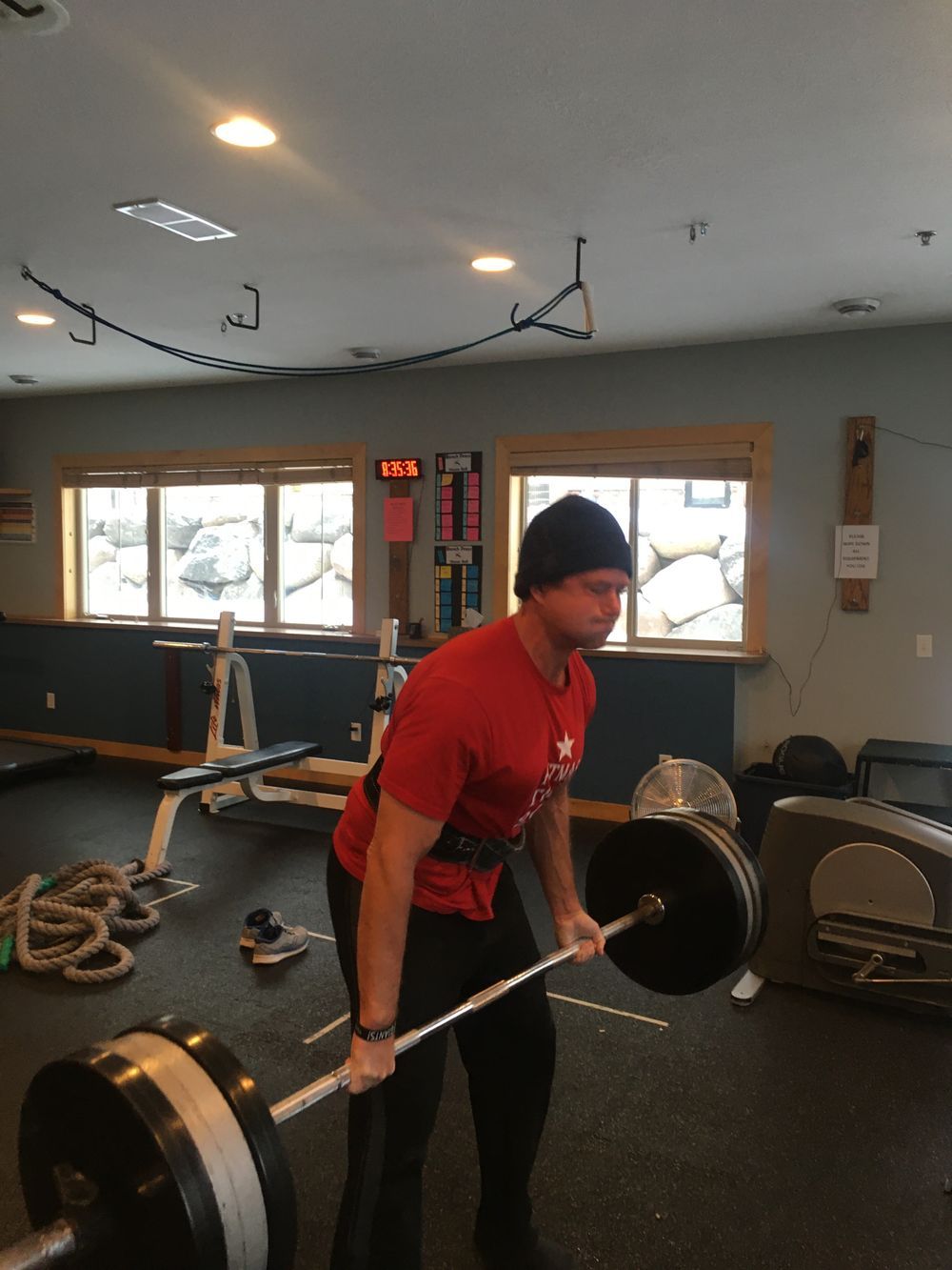 A man in a red shirt is lifting a barbell in a gym