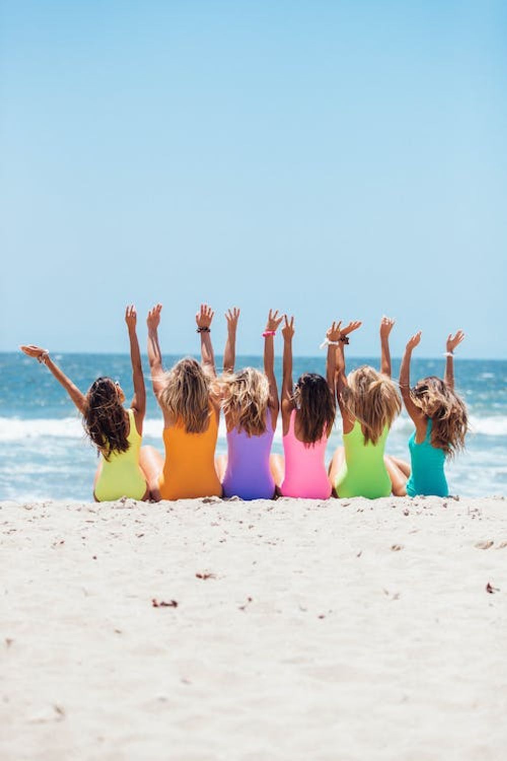 A group of women are sitting on the beach with their arms in the air.