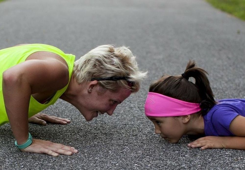 A woman and a girl are doing push ups on the ground.