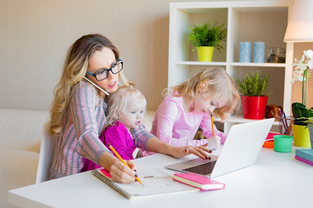 A woman is sitting at a table with two children and talking on a cell phone.