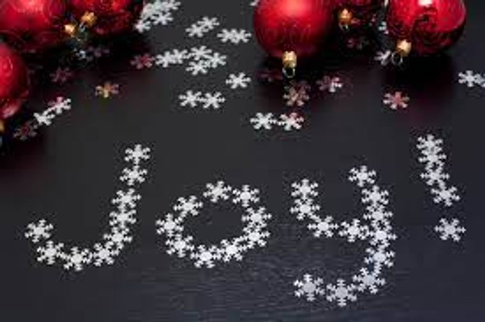 The word joy is written with snowflakes on a black surface surrounded by christmas decorations.