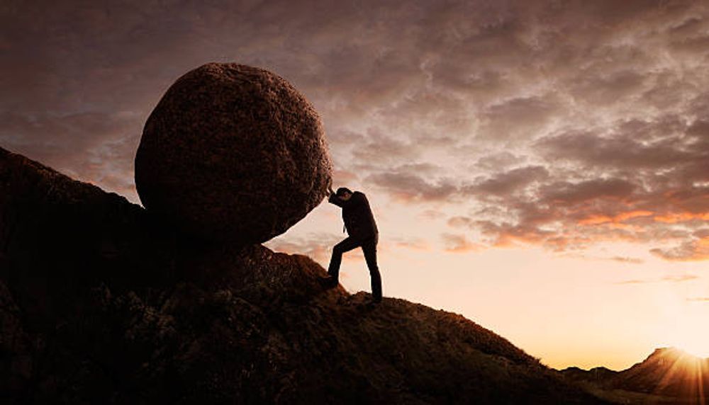 A man is pushing a large rock up a hill.