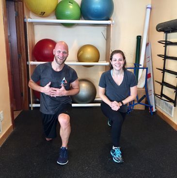 A man and a woman are squatting in front of a shelf of exercise balls