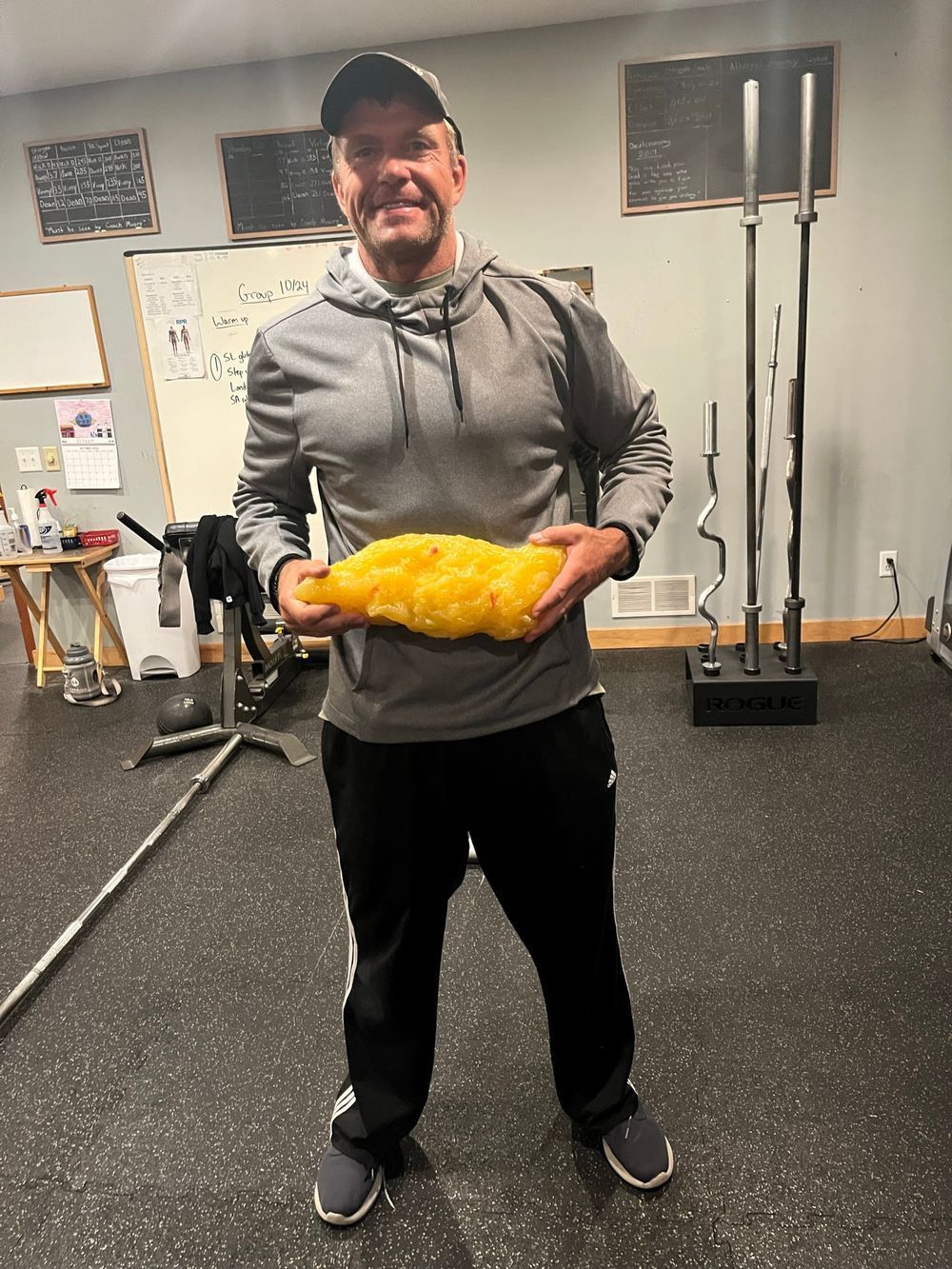 A man is holding a large yellow object in a gym.