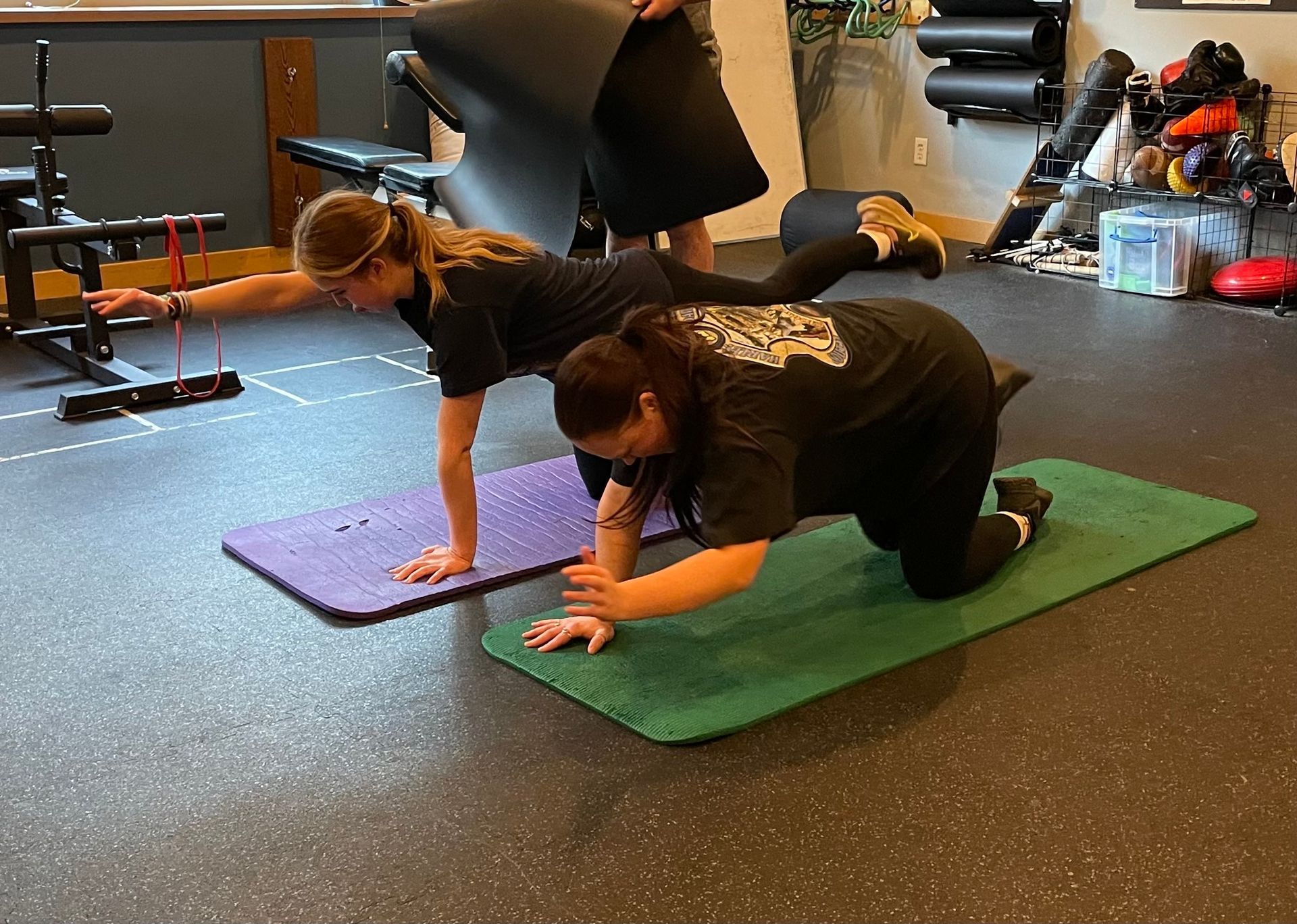 Two women are doing push ups on yoga mats in a gym.