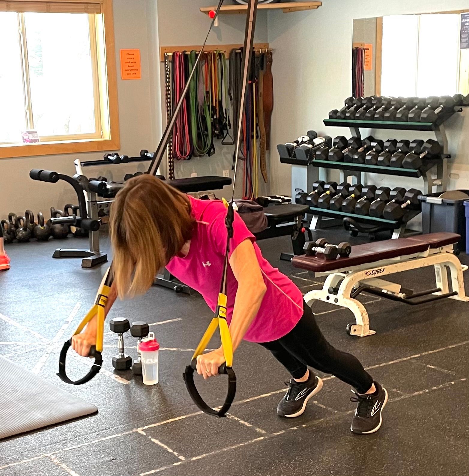 A woman in a pink shirt is doing trx exercises in a gym