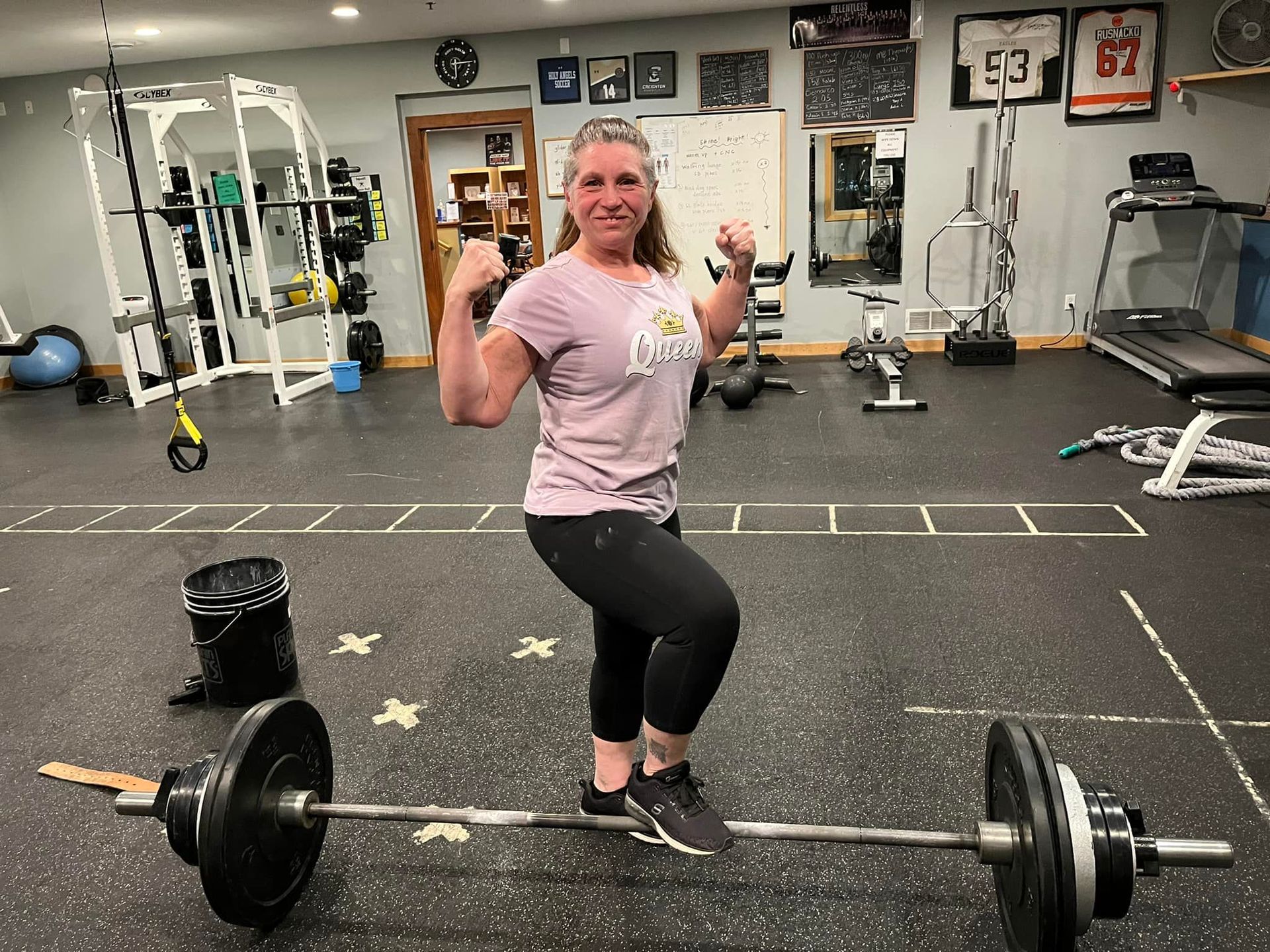 A woman is standing on a barbell in a gym.