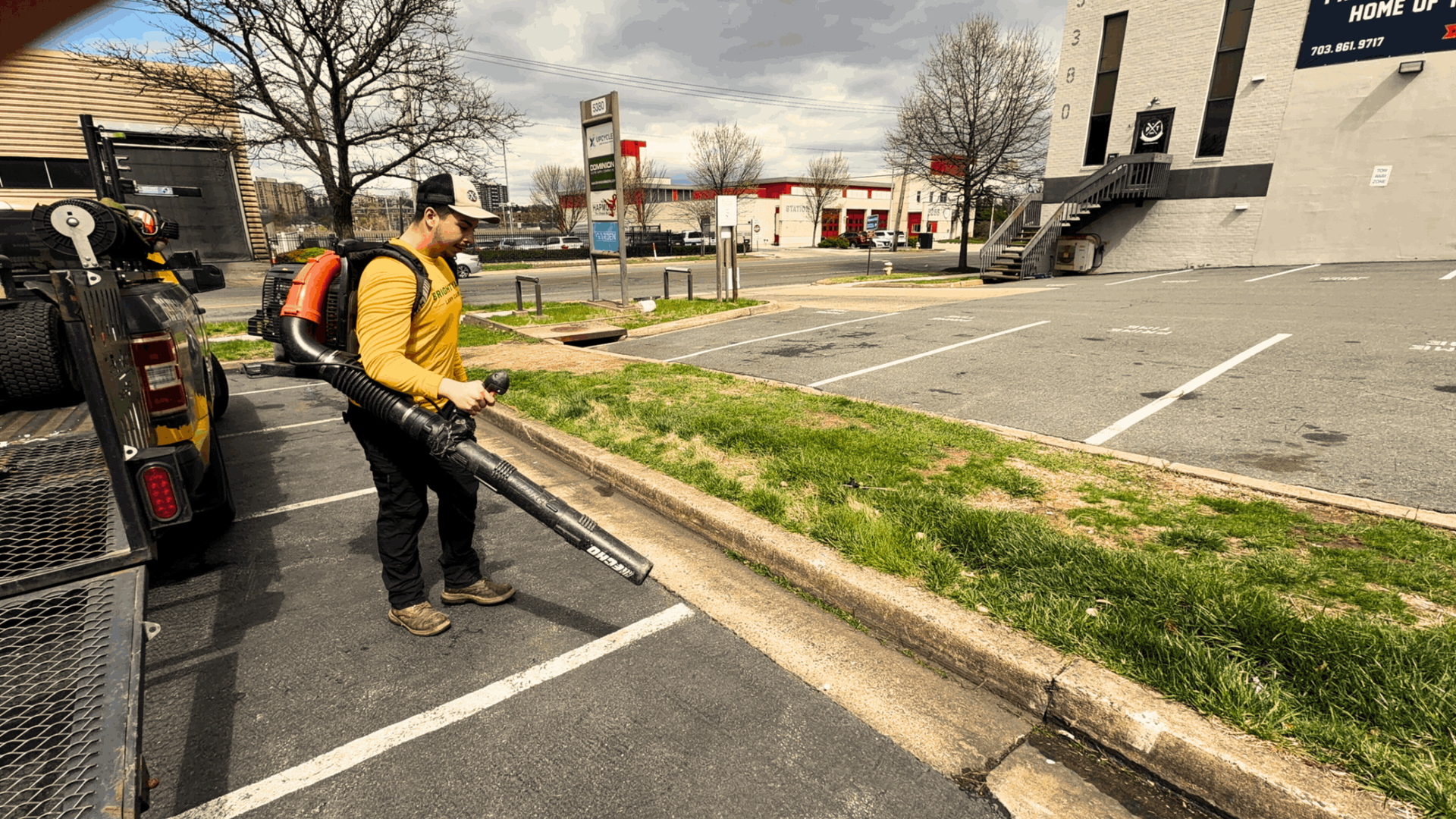 Man using leaf blowers to clear fallen autumn leaves in a grassy park setting.
