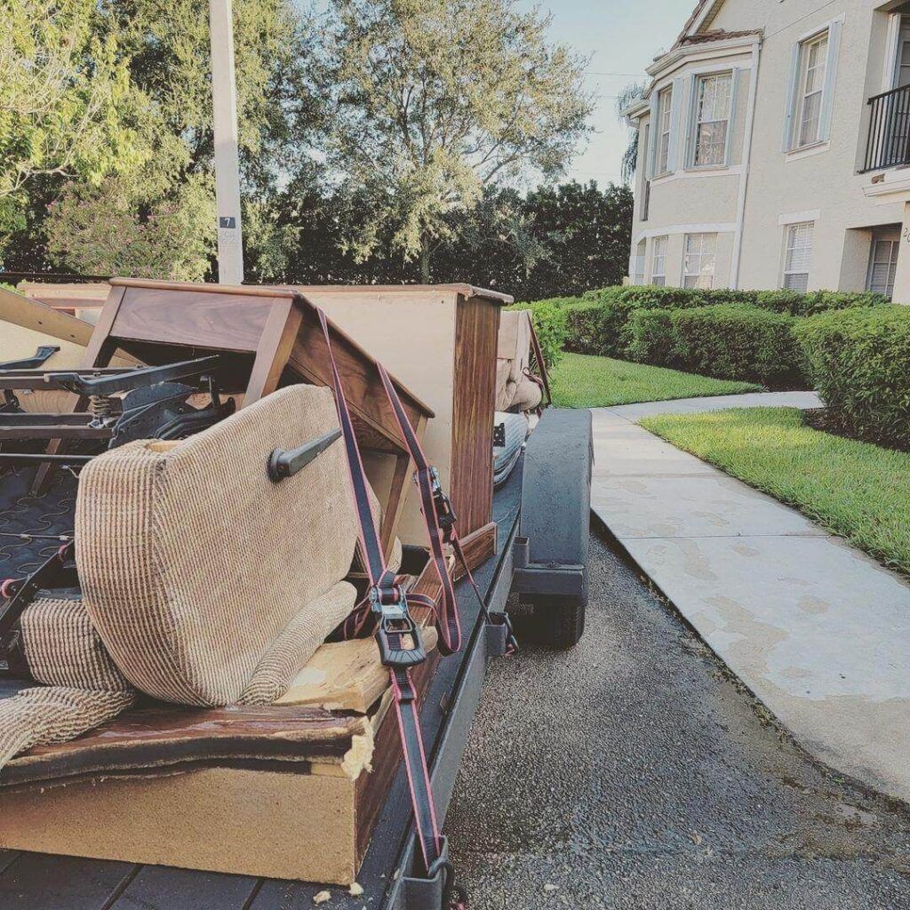Trailer loaded with boxes in a driveway beside a blue SUV and garage