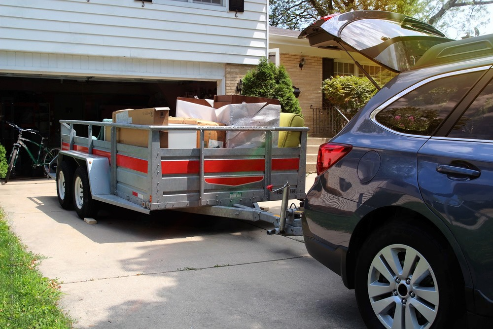 Trailer loaded with boxes in a driveway beside a blue SUV and garage