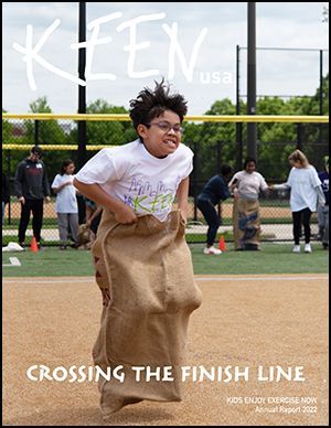 Boy in KEEN Tee Shirt hopping in gunny sack at outdoor field