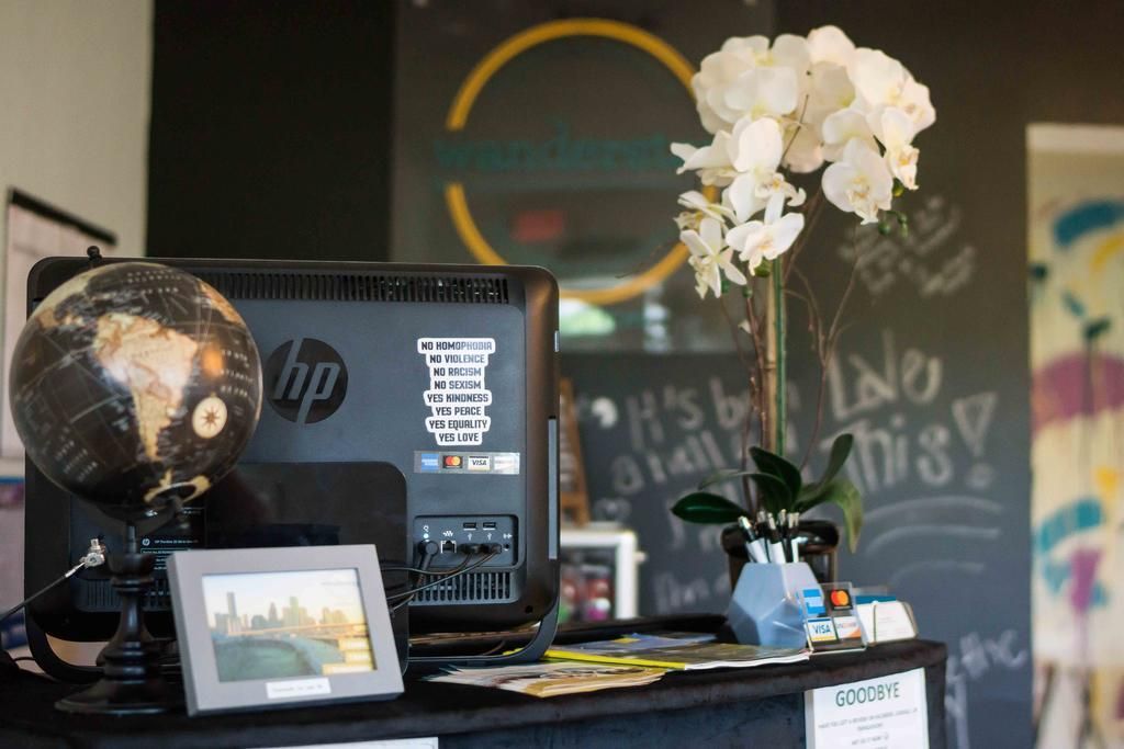 Desk with computer, globe, and flowers in front of a dark wall with colorful artwork and a sign.