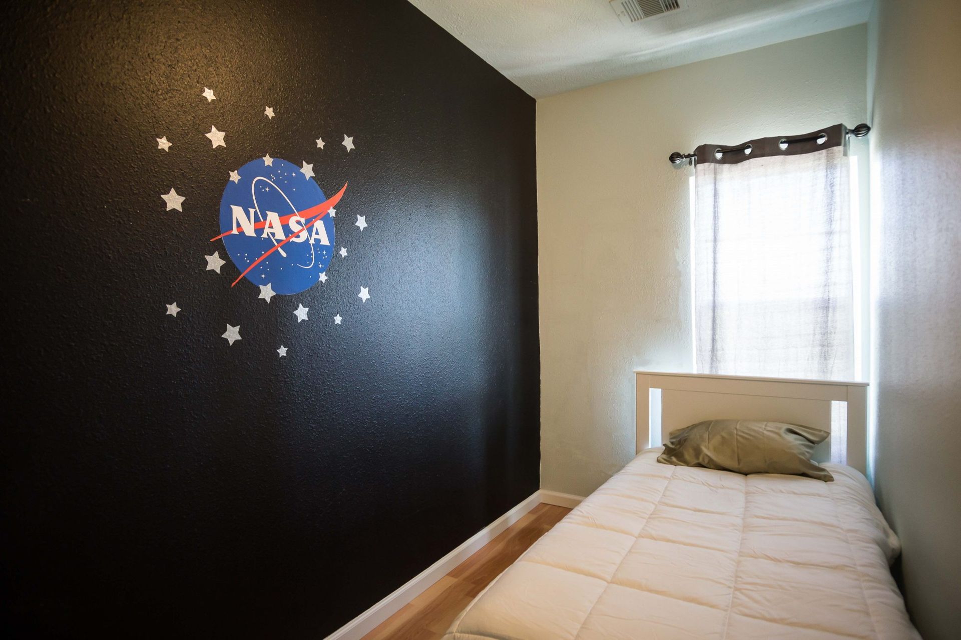 Black accent wall with a NASA logo, twin bed in a room with a small window.