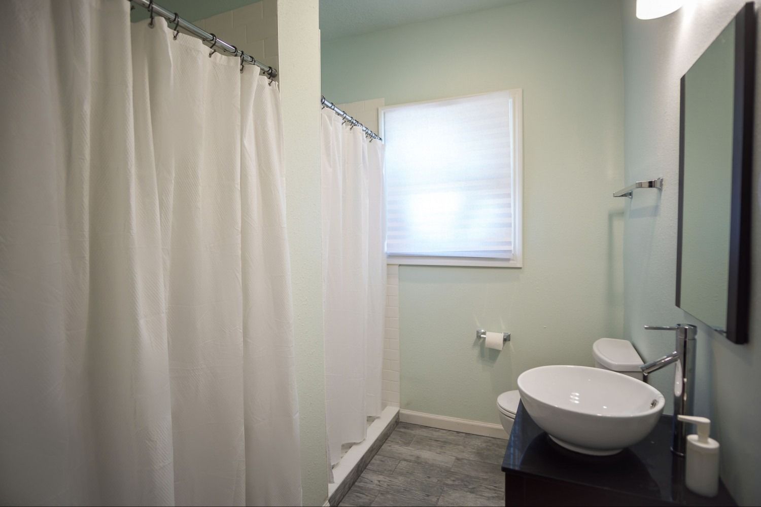 Bathroom with white shower curtain, sink, toilet, and window. Light green walls.
