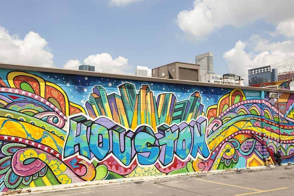 Colorful Houston mural featuring the city skyline, against a cloudy blue sky.