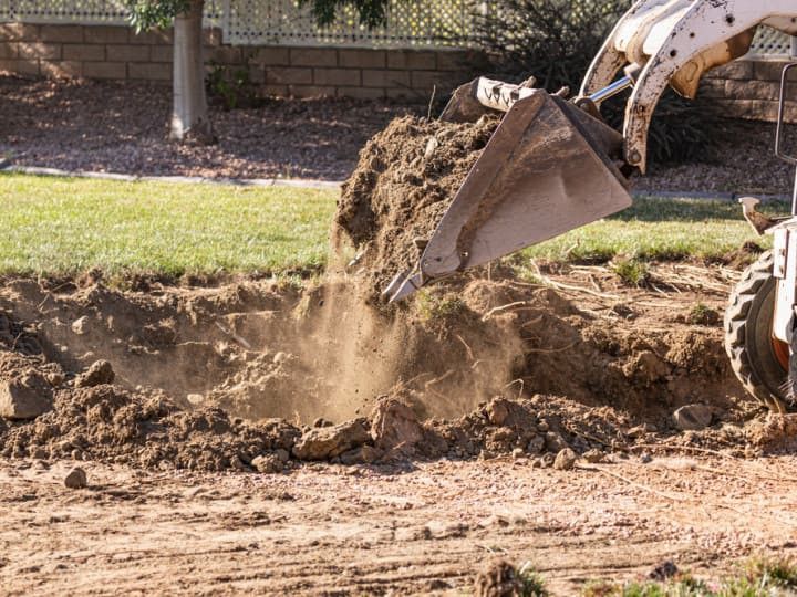 Bobcat excavator dumping dirt into a trench on a sunny day.