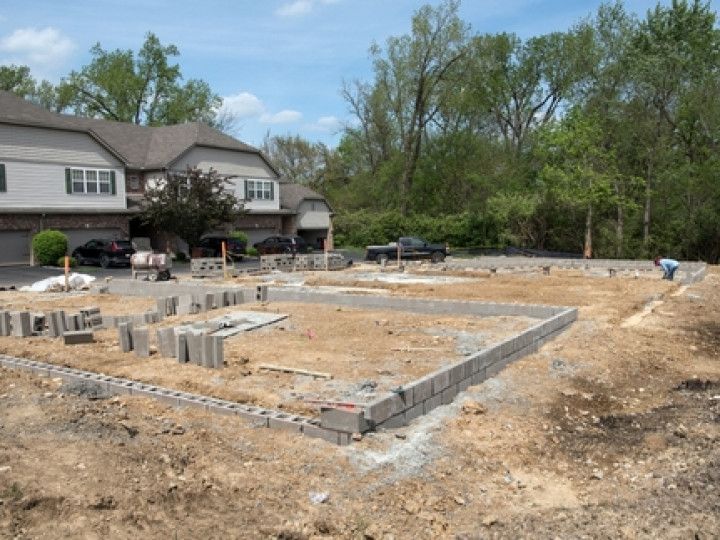 Construction site with concrete block foundation laid out in front of a multi-unit dwelling.