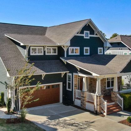 Two-story house with dark blue siding, brown garage door, and a covered porch with stone accents.