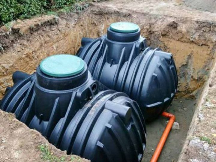 Two black plastic septic tanks buried in a trench, with an orange pipe visible.