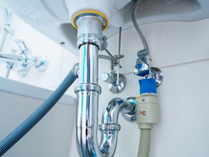 Plumbing under a sink: chrome pipes, faucet, water supply valves, and a drain hose.