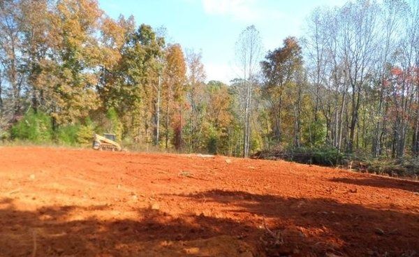 Cleared red earth field with trees in the background under a blue sky.