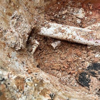Close-up of a broken white pipe in a hole filled with brown dirt and chunks of soil.