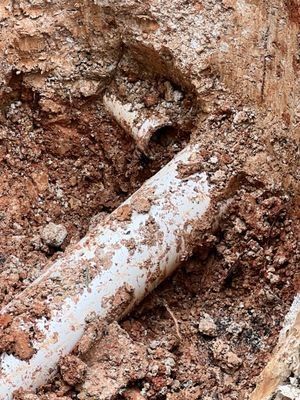 White PVC pipes exposed in a dirt trench, likely for plumbing or drainage purposes.