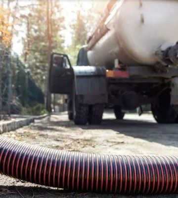 A large truck with a tank and hose on a road, likely servicing a septic system.