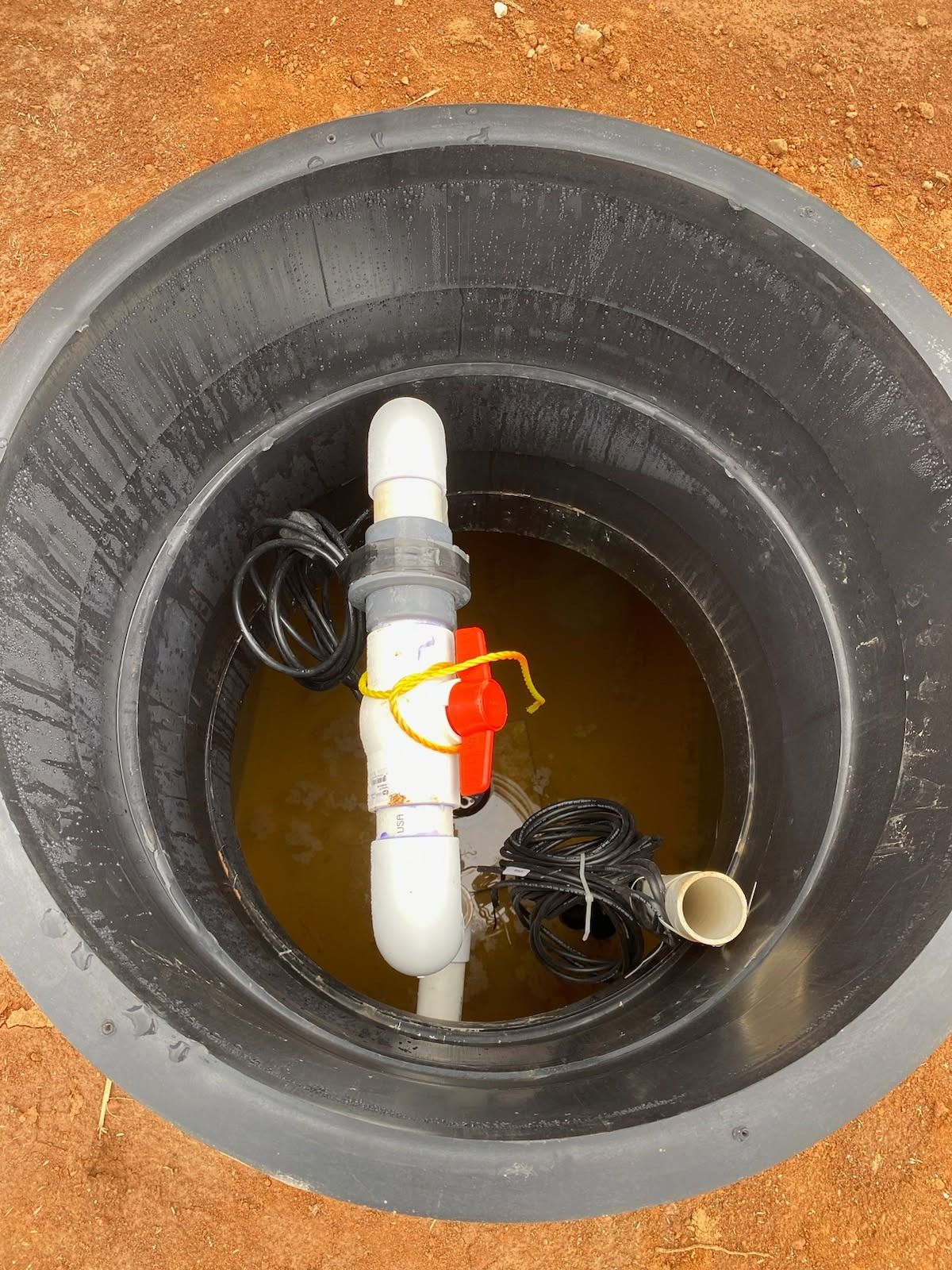 Black tank with water and white PVC pipe, red valve, and black electrical wires.