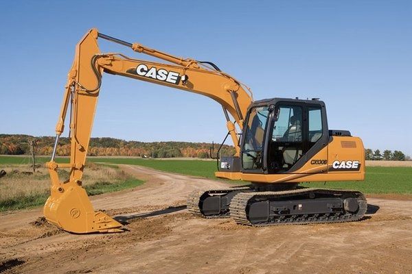 Yellow Case excavator on dirt, arm extended, on a field with blue sky.