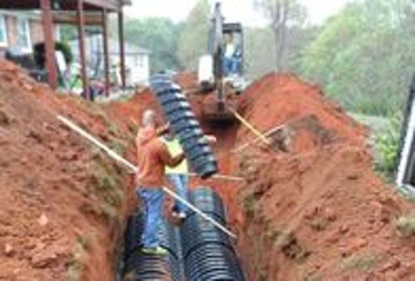 Construction workers installing corrugated black drainage pipes in a trench.