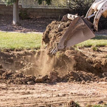 A backhoe dumping dirt from its bucket into a ditch in a grassy area.