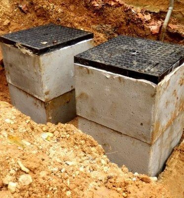 Two concrete utility boxes with black, gridded lids are partially buried in dirt.