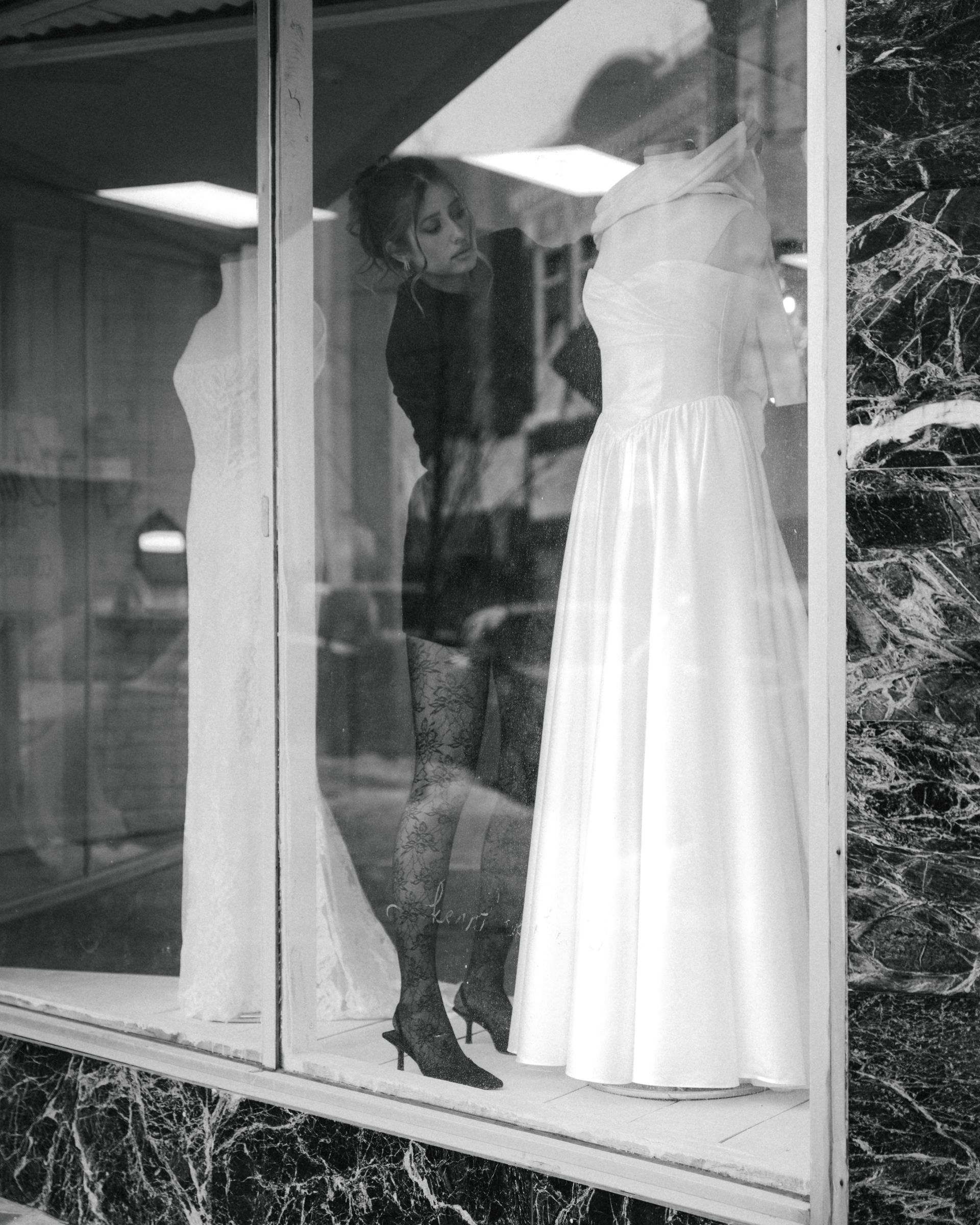 A woman is looking at a wedding dress in a store window