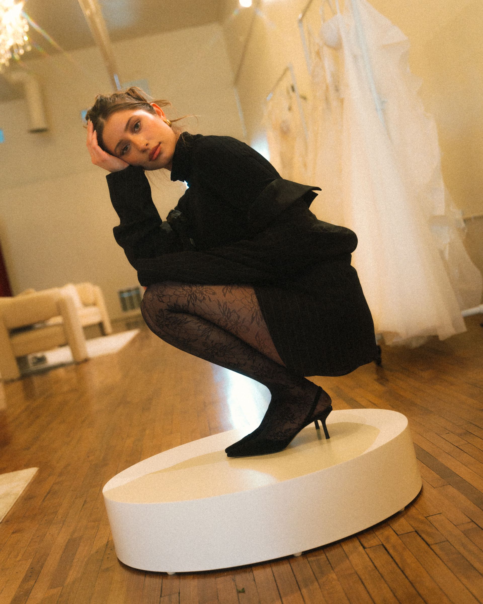 A woman squatting on a white pedestal in a room