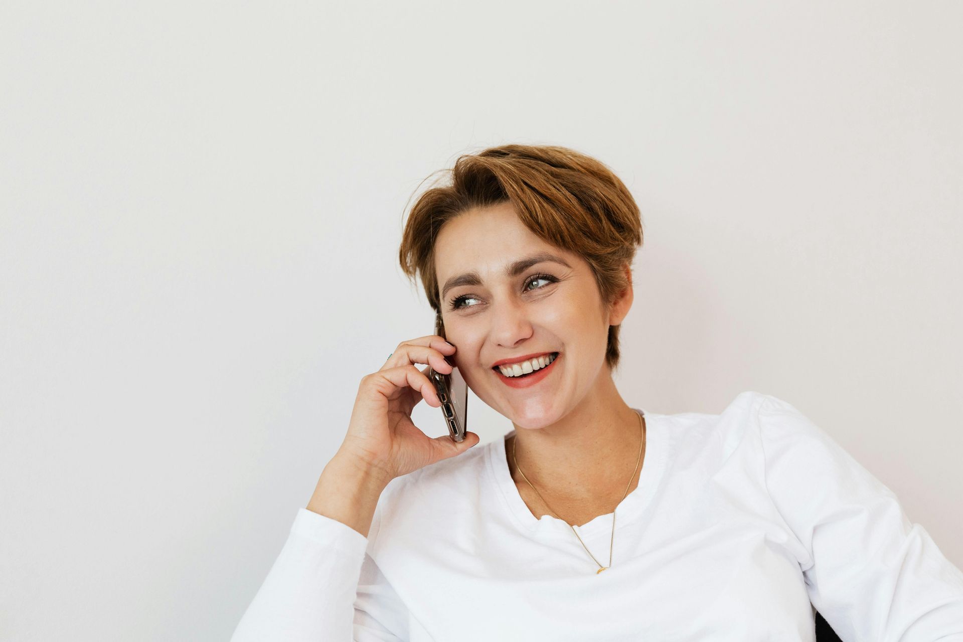 A woman is smiling while talking on a cell phone.