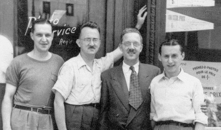 quatre hommes posent pour une photo devant une fenêtre avec le mot service écrit dessus
