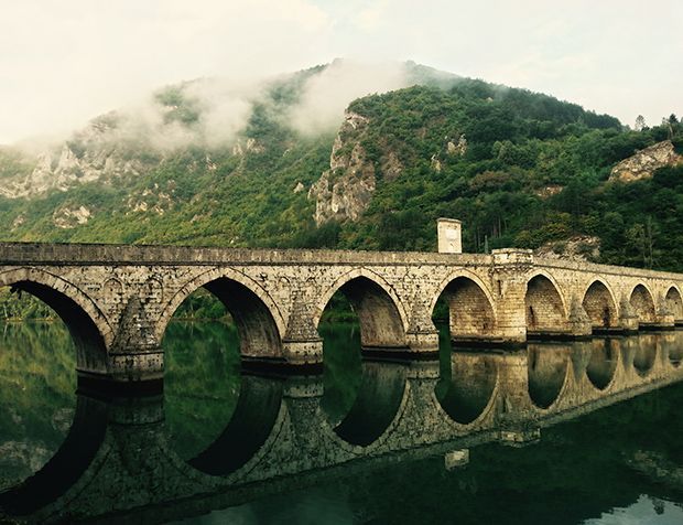 un vieux pont en pierre sur un lac avec des montagnes en arrière-plan .