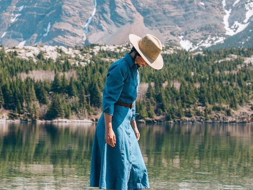 a woman in a denim dress and hat is standing in a lake