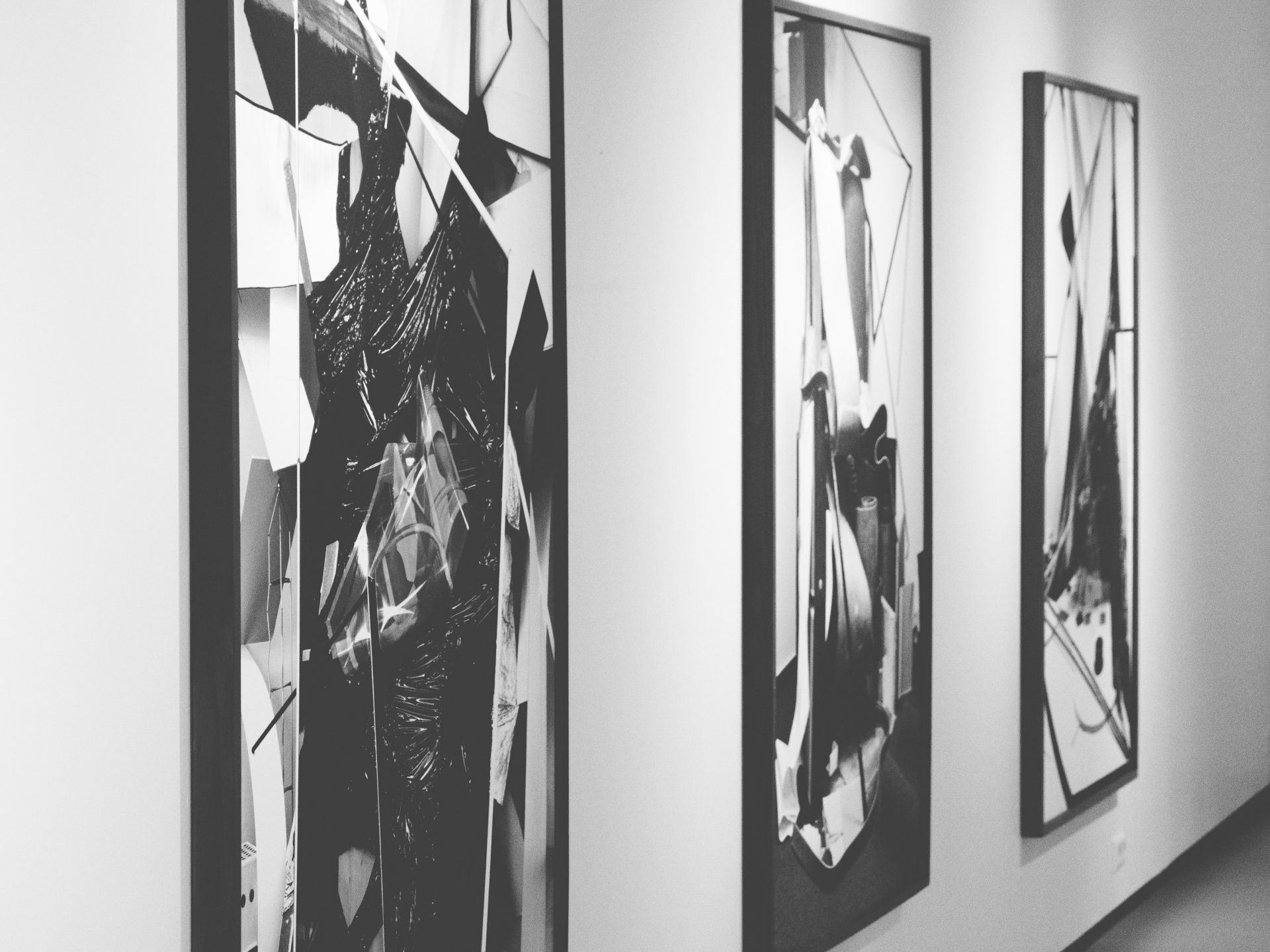 three black and white paintings hang on a white wall