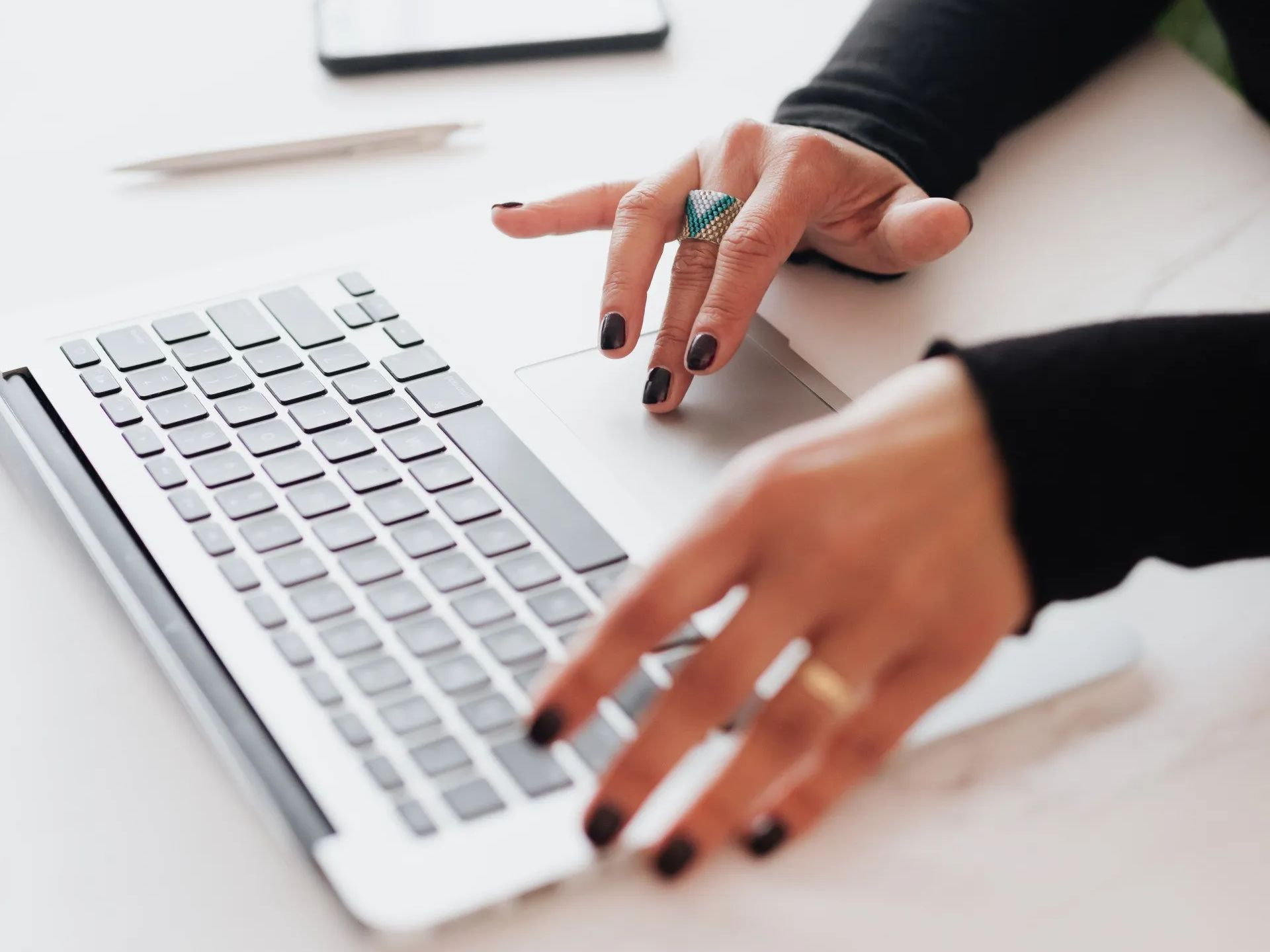 a woman with black nails is typing on a laptop