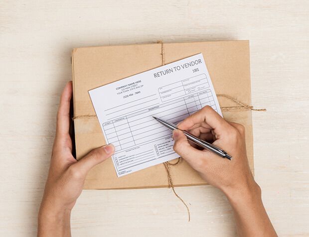 a person is writing on a return to vendor form next to a box .