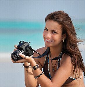 a woman in a bikini is holding a camera on the beach .