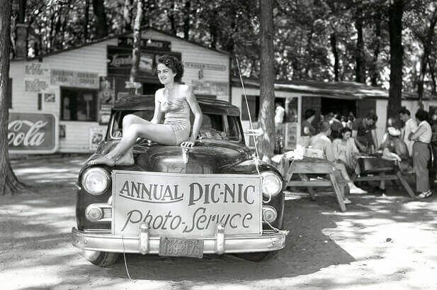 une femme en maillot de bain est assise sur le capot d' une voiture .